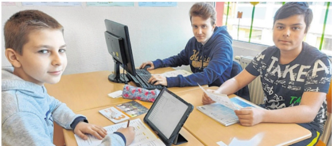 Foto aus den Schleswiger Nachrichten. Drei Schüler sitzen im Unterrichtsraum uns arbeiten mit analogen und digitalen Lehrmitteln. 